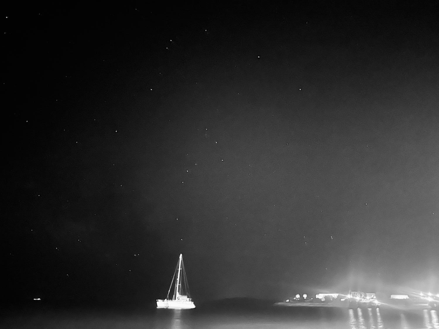 A starry night view over the sea with a sailing boat anchored in Piso Livadi, Paros. Nighttime star gazing and exploring the coastal towns are key activities when deciding what to do in Paros.