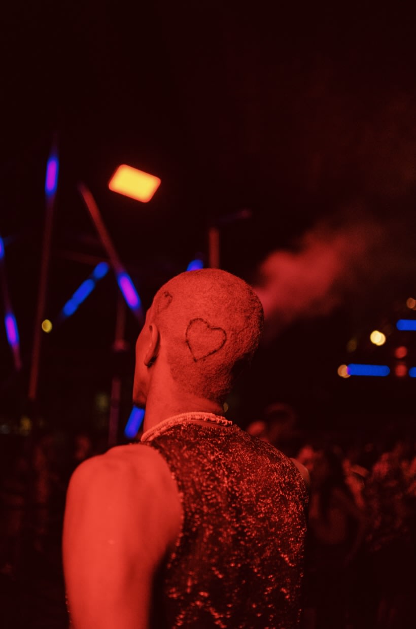 A person with a heart-shaped design shaved into their hair, illuminated by red lights in a gay club in Porto, exemplifying the lively nightlife of gay Porto.