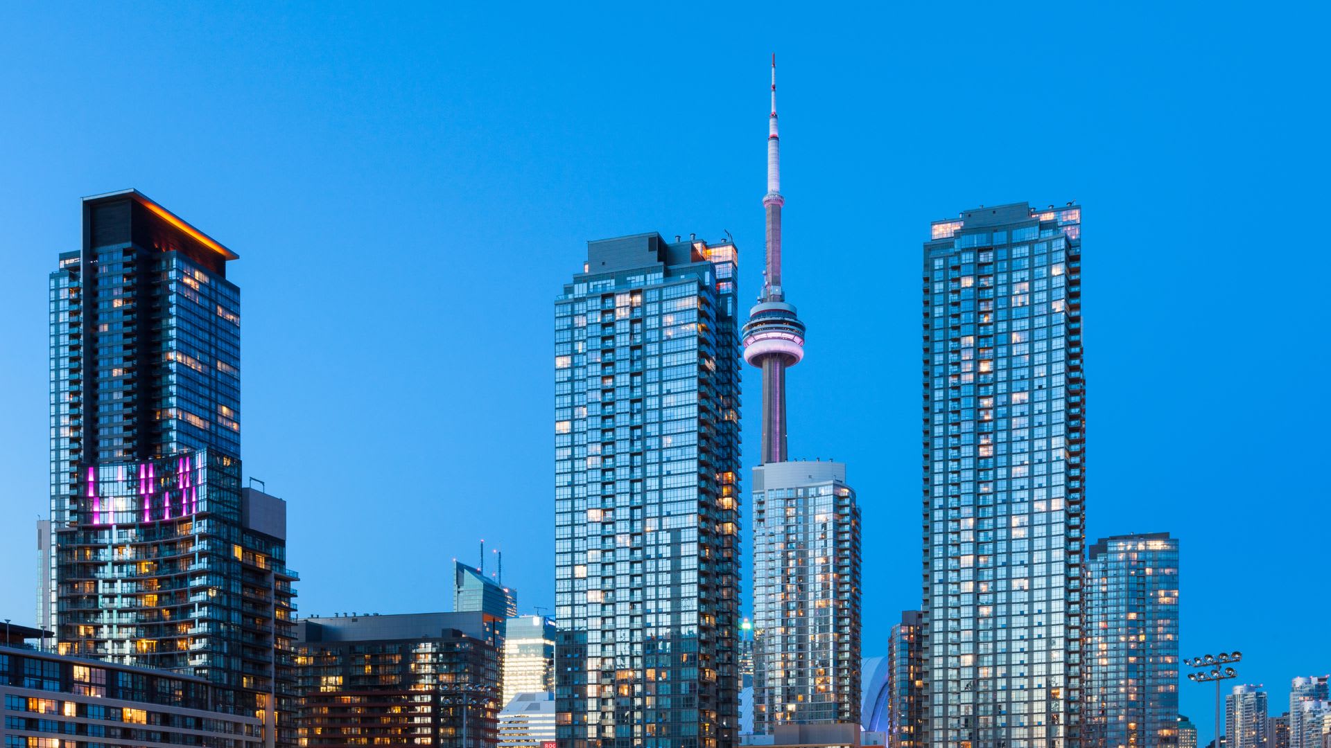 In the breathtaking skyline during twilight, modern skyscrapers glisten with their glass-clad exteriors reflecting the fading light. Among them, a tall tower with a needle-like spire stands out, shining brightly in the urban silhouette. Toronto evokes the essence of LGBTQ+ friendly countries that are increasingly popular among Americans seeking vibrant destinations to relocate abroad. As you gaze upon this illuminated metropolis, countries like Canada, known for its inclusive policies.