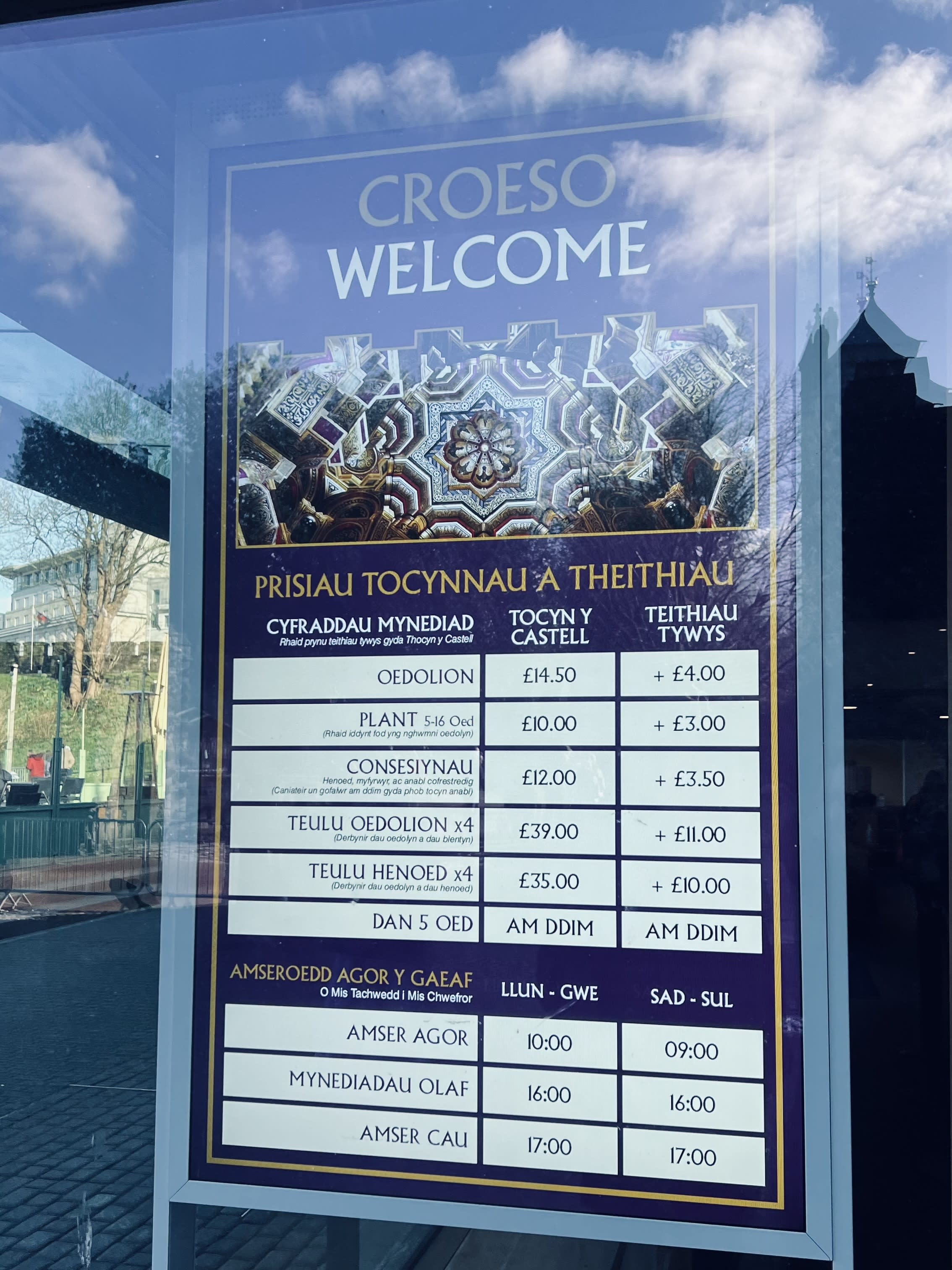 Welcome sign with ticket prices and visiting hours for a majestic castle in Wales, gracefully displayed in both Welsh and English, offering a perfect guide for visitors exploring nearby cozy cottages. Add this to your Wales itinerary to ensure you don't miss the enchanting blend of history and charm on your journey.