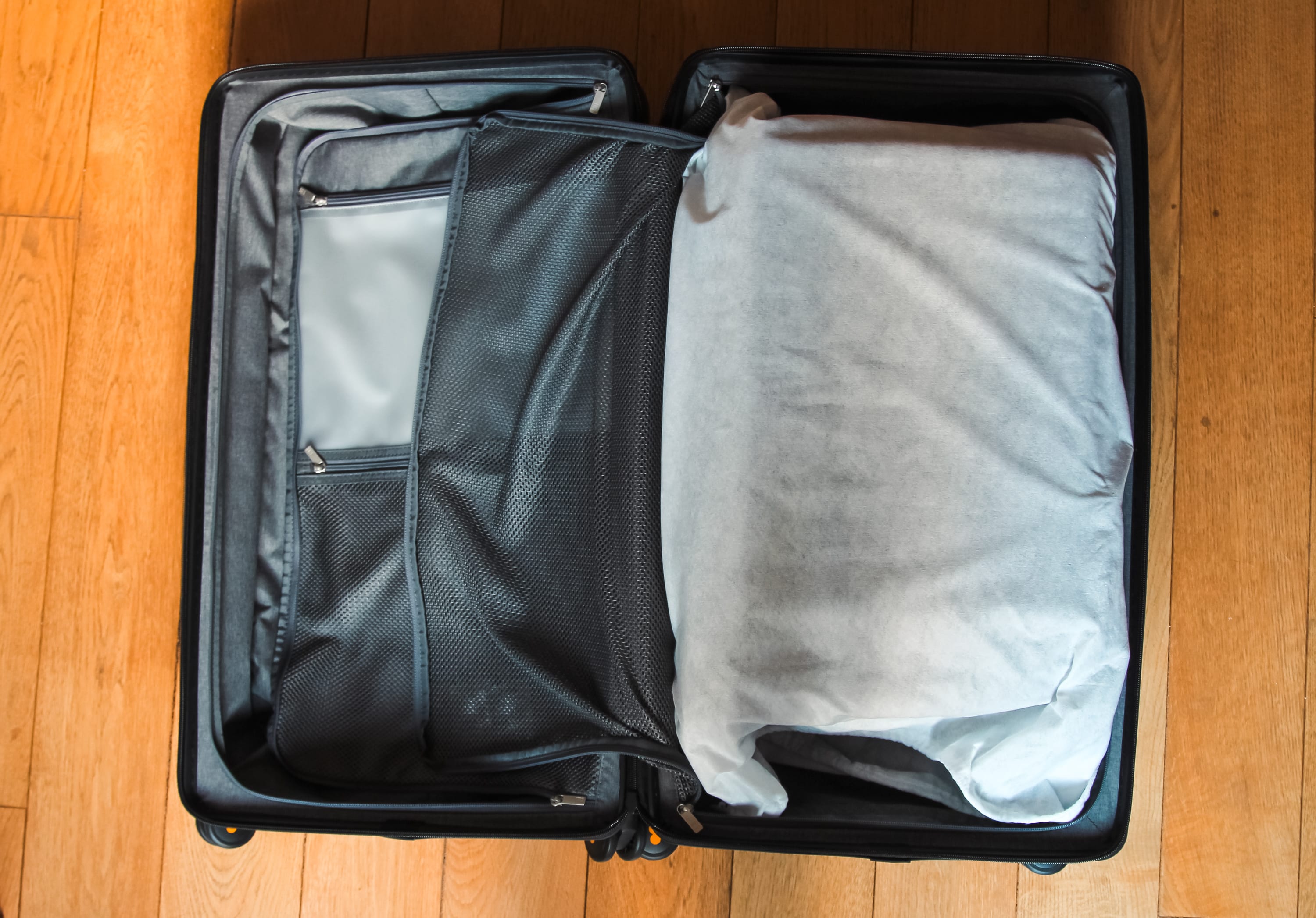 An open LEVEL8 Road Runner suitcase sits on a wooden floor, with a large white garment bag inside and mesh pockets visible on the left—perfect for digital nomads seeking organization and style in their durable suitcases.