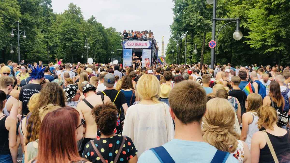 A sea of participants at a gay pride march in Berlin's Tiergarten, with vibrant flags and banners, as individuals come together to stand for equality and LGBTQ+ rights.