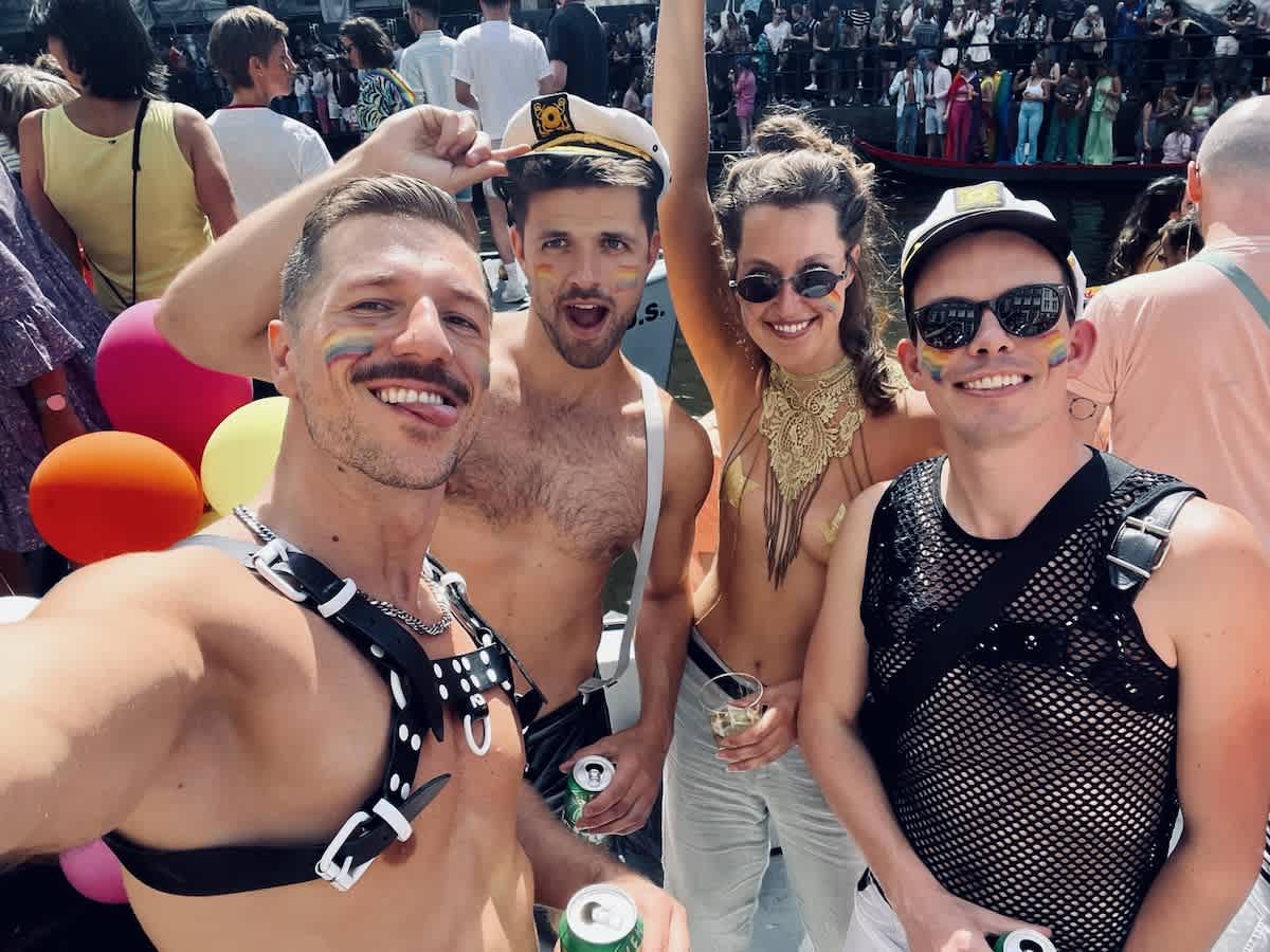 A joyful selfie capturing the essence of gay pride in Amsterdam, with four friends donning pride colors and playful outfits, sharing smiles and pride at a festive event on a boat.