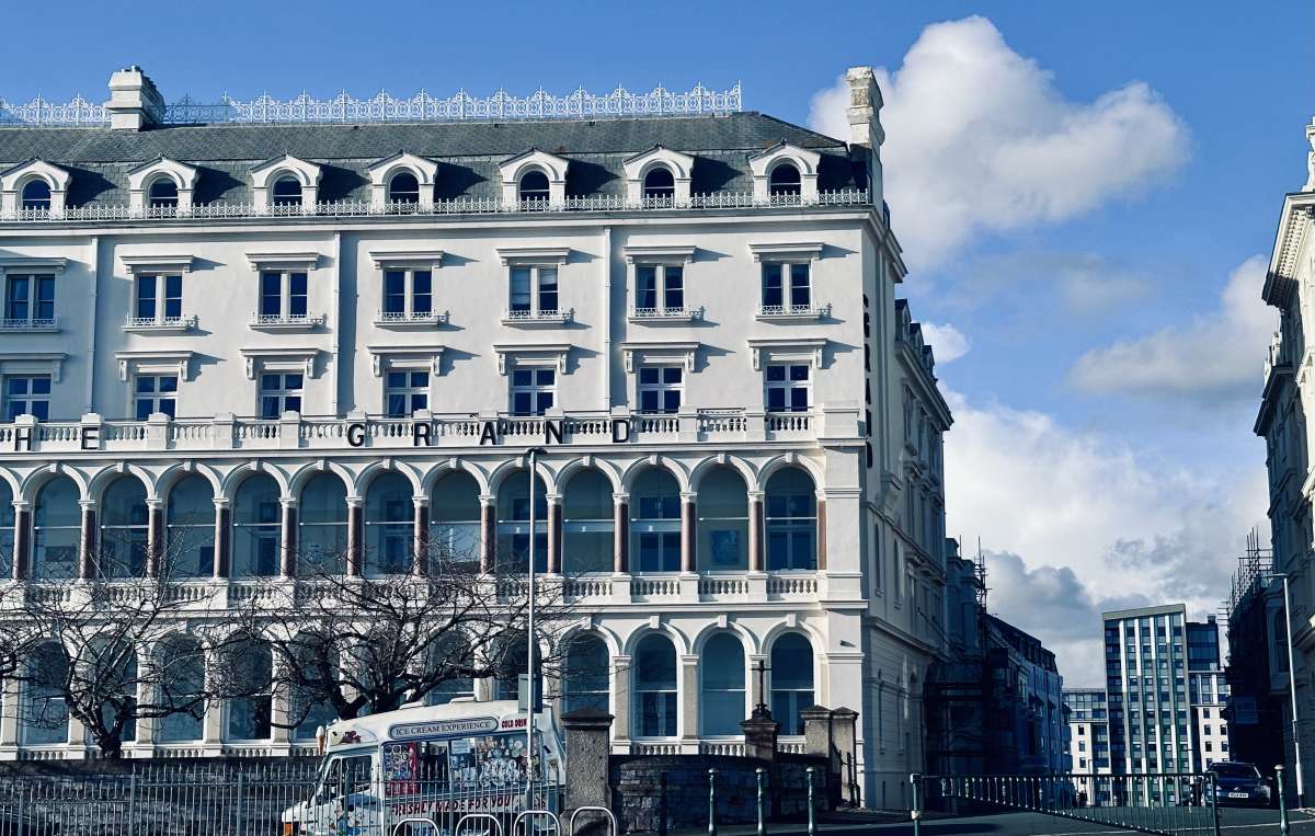 A classic Victorian building in Plymouth with intricate ironwork balconies under a bright blue sky, contrasted by modern architecture in the distance.