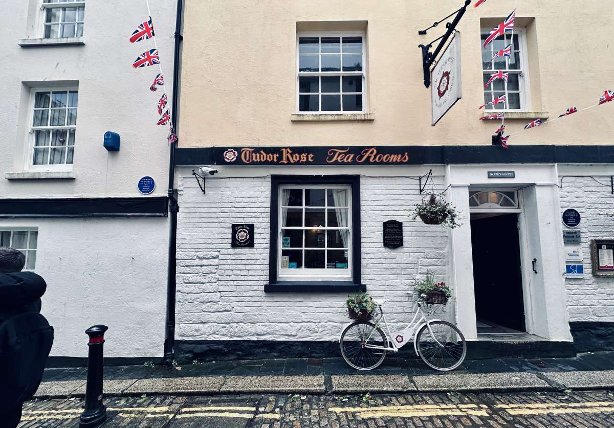 Charming street view of Tudor Rose Tea Rooms in Plymouth, distinguished by its white façade and quaint decorations, including a vintage bicycle and hanging Union Jack bunting, evoking a quintessentially British atmosphere.