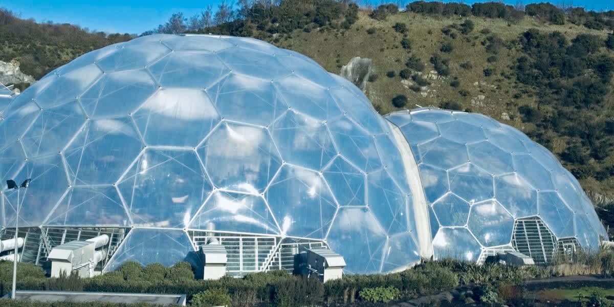 The distinctive biomes of the Eden Project in Cornwall, with their geodesic dome structures, nestled in a natural valley under a clear blue sky, reflecting the project's dedication to environmental education.