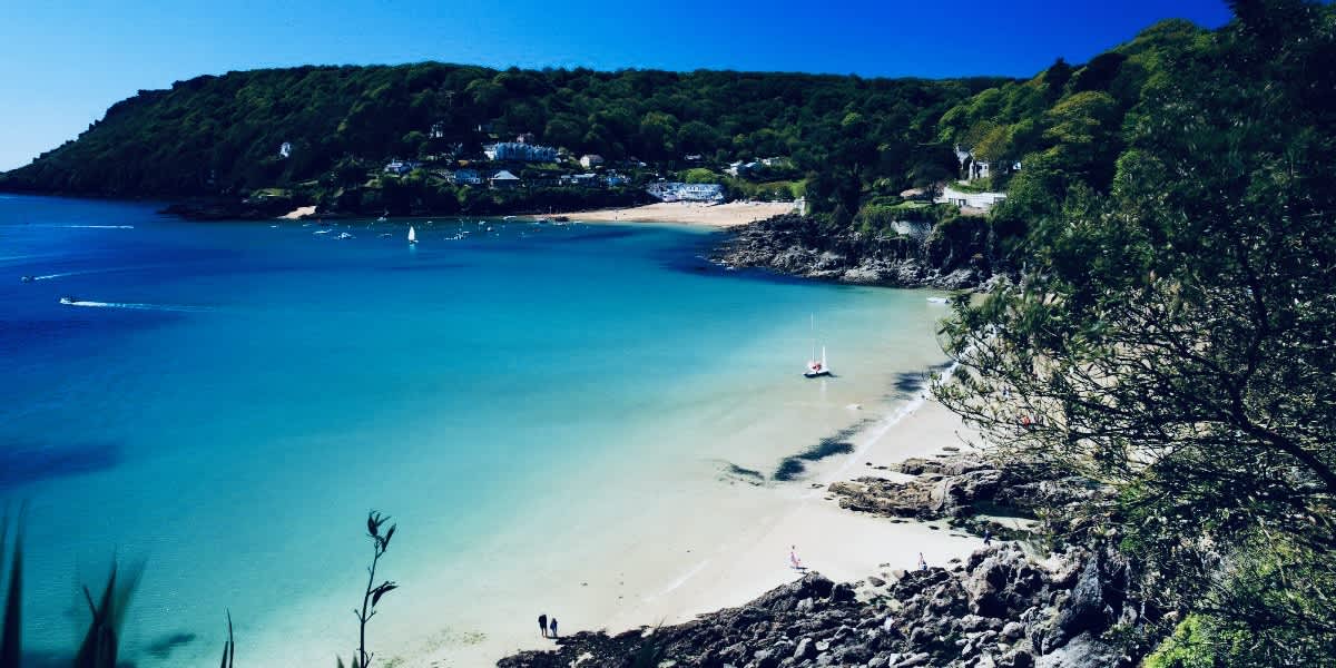 Stunning view of Salcombe, with its turquoise waters and sandy beach bordered by lush greenery, a quintessential South Devon haven for beach-goers and sailing enthusiasts on a sunny day.