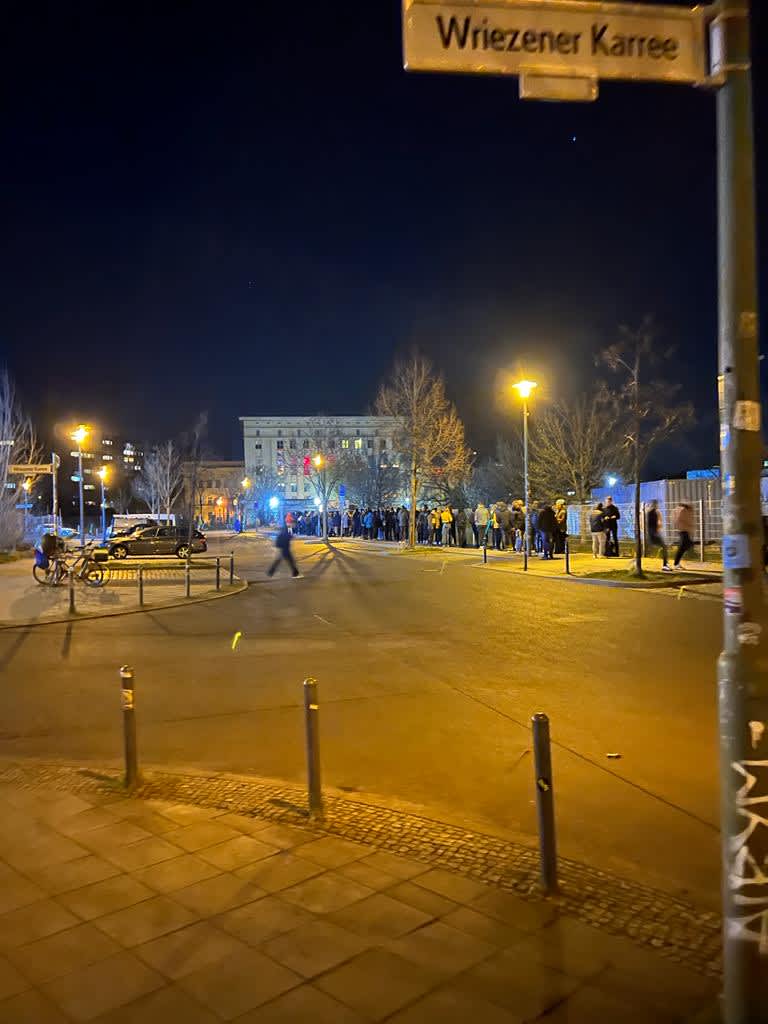 Nighttime scene of a long queue at Berghain, Berlin's renowned nightclub, with eager attendees lining up on Wriezener Karree under street lights, reflecting the city's legendary nightlife culture.