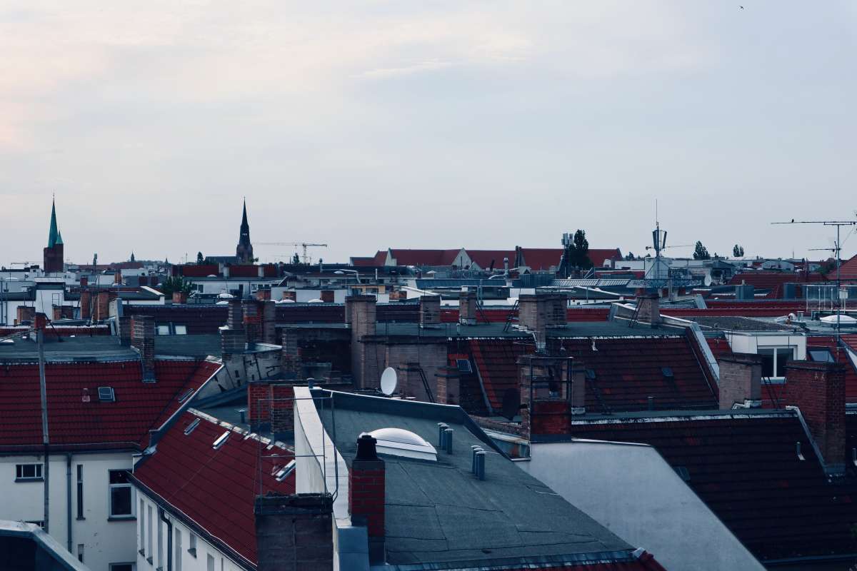 The iconic sea of red Altbau rooftops in Friedrichshain, Berlin, during dusk, with the silhouette of church spires piercing the skyline, illustrating the historic charm of the neighborhood.