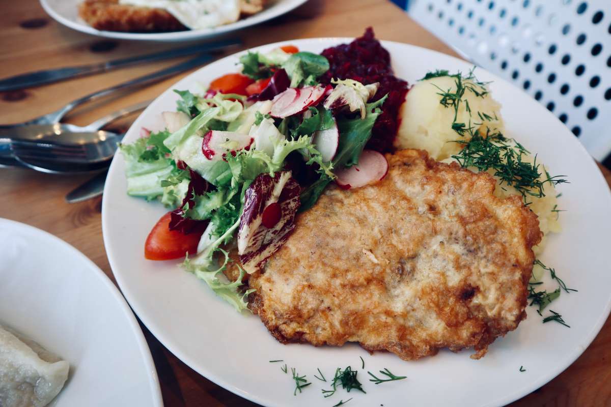 Close-up of a crispy breaded cutlet paired with mashed potatoes and a refreshing mixed salad at the best milk bar in Warsaw, highlighting the traditional Polish cuisine.