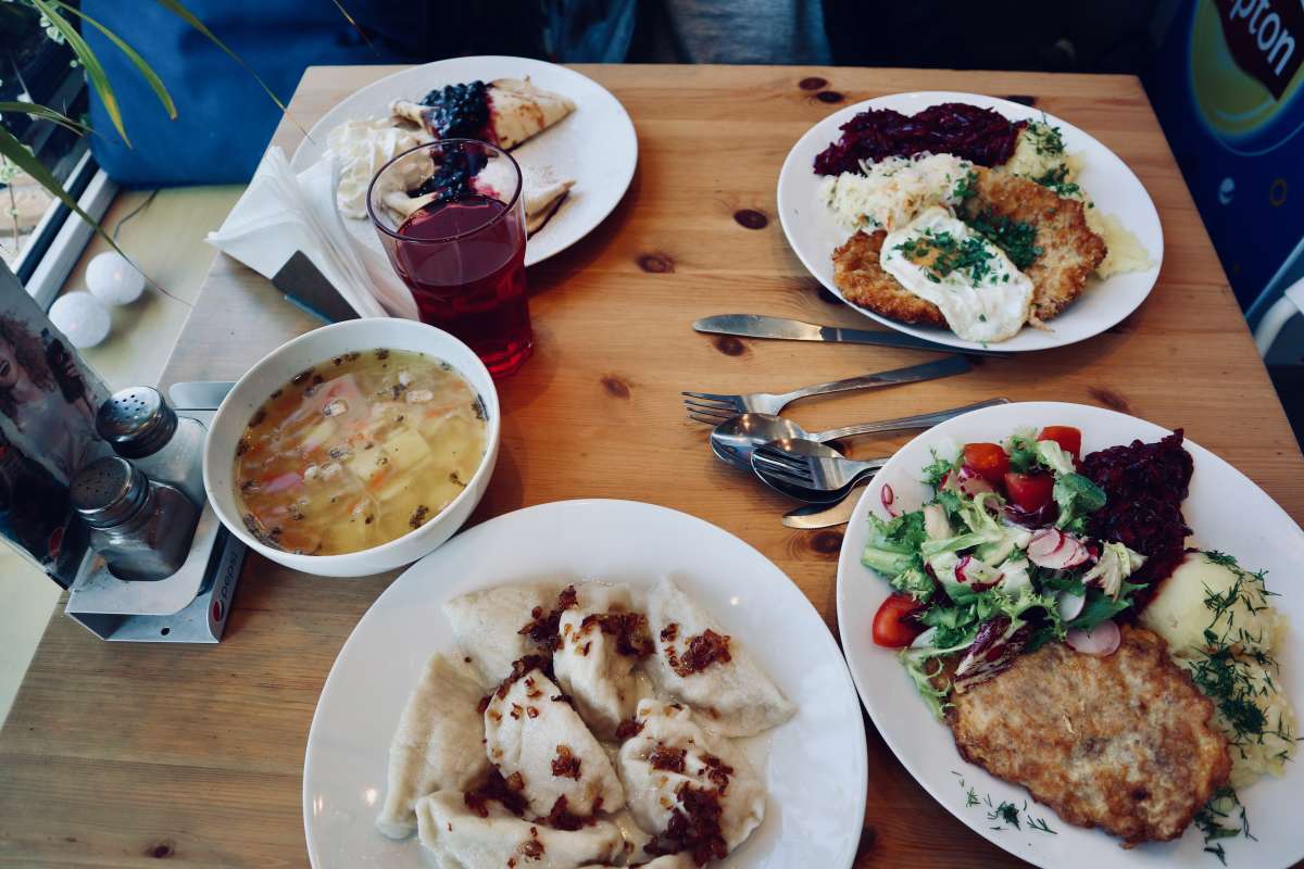 A full spread of Polish culinary delights at Warsaw's premier milk bar, showcasing soup, pierogi with a side of sour cream, a schnitzel with mashed potatoes and garnished with dill, and a colorful salad.