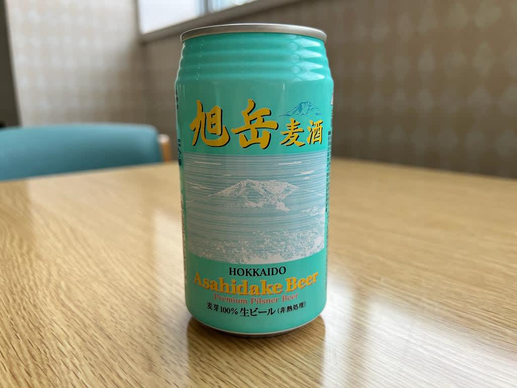 A can of Asahidake Beer on a table, with Japanese characters and an illustration of a mountain, a local beverage to try on a Hokkaido itinerary.