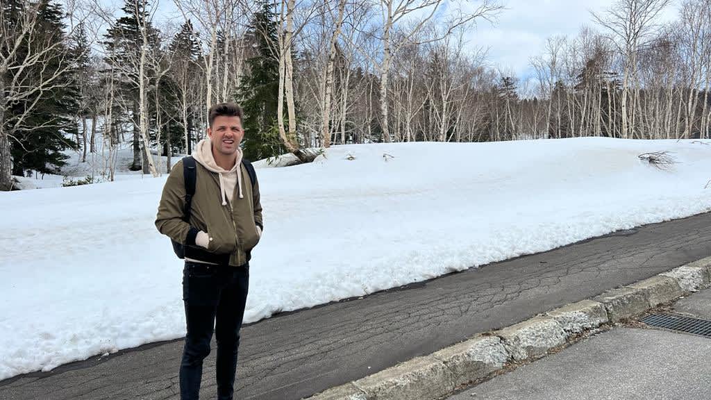 A traveler standing against a backdrop of snow-covered ground and trees near Mount Asahidake, highlighting winter activities in a Hokkaido itinerary