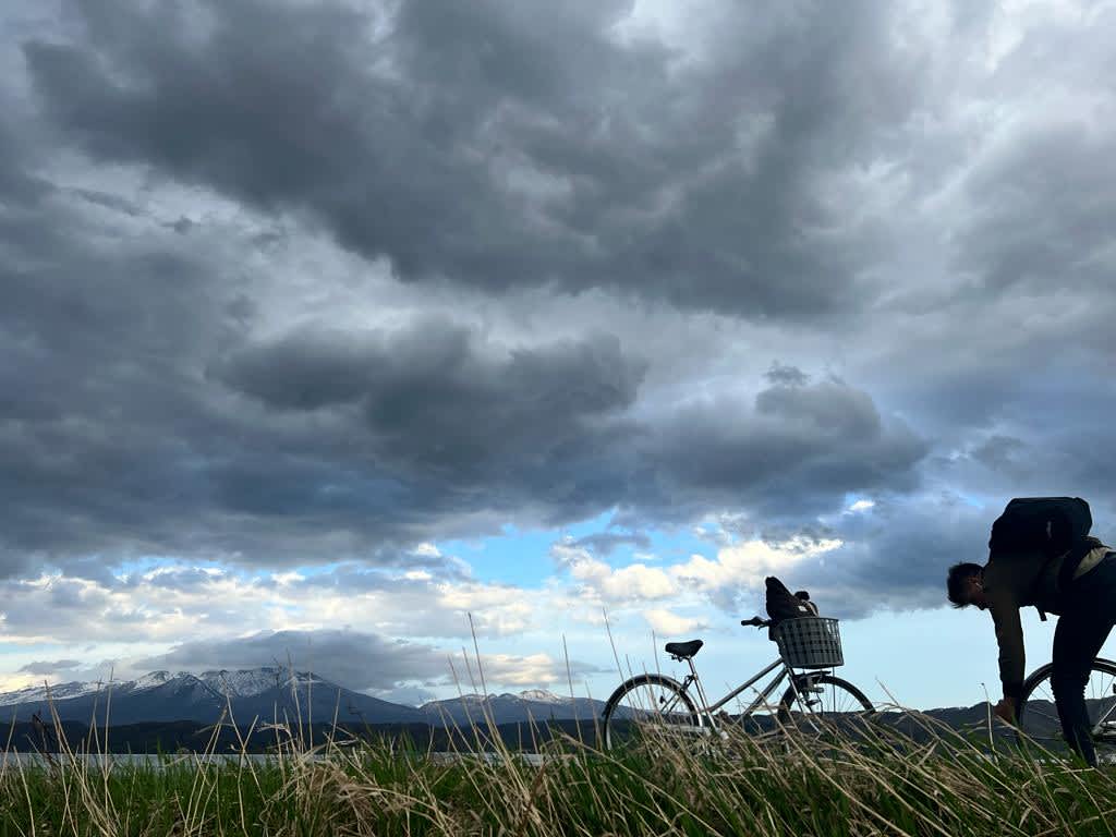 A dramatic sky with storm clouds over the plains of Hokkaido as two people prepare for a bike ride, an example of the dynamic weather encountered on a Hokkaido itinerary.