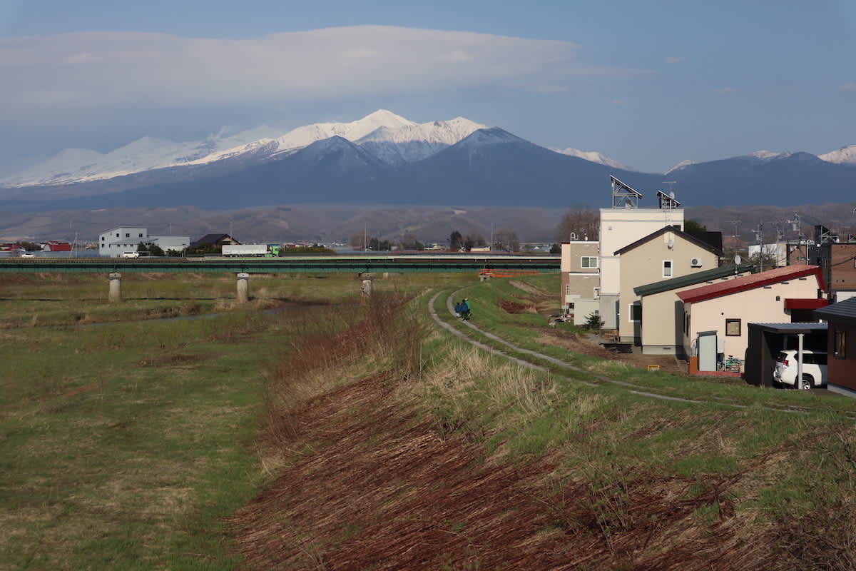 A picturesque scene in Furano, Hokkaido, with a house foregrounding the expansive view of the distant, snow-covered mountains, a tranquil sight on a Hokkaido itinerary.