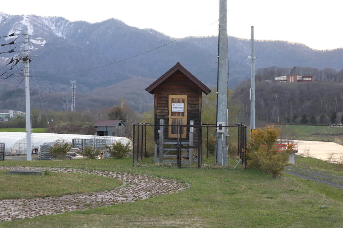 A small wooden electricity distribution hut in rural Hokkaido, with a mountainous backdrop and the last traces of snow, illustrating the rustic charm of the island.