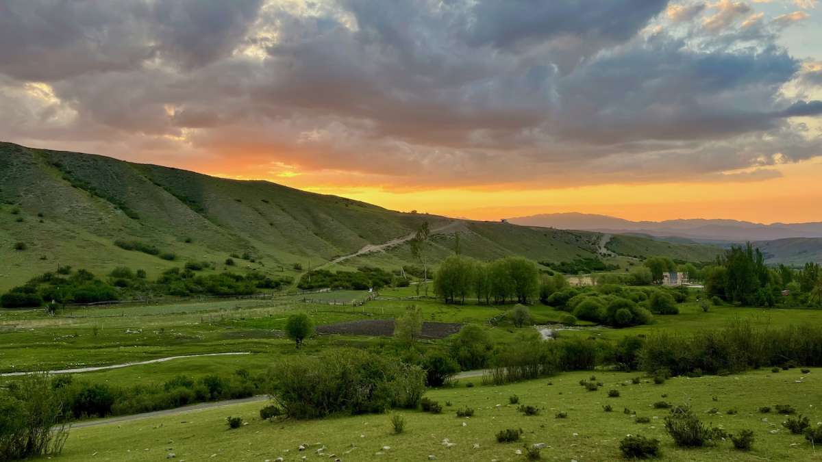 A breathtaking sunset over the hills of Karabulak in Kazakhstan, illuminating the sky in warm hues, showcasing a perfect stop for travelers on a road trip