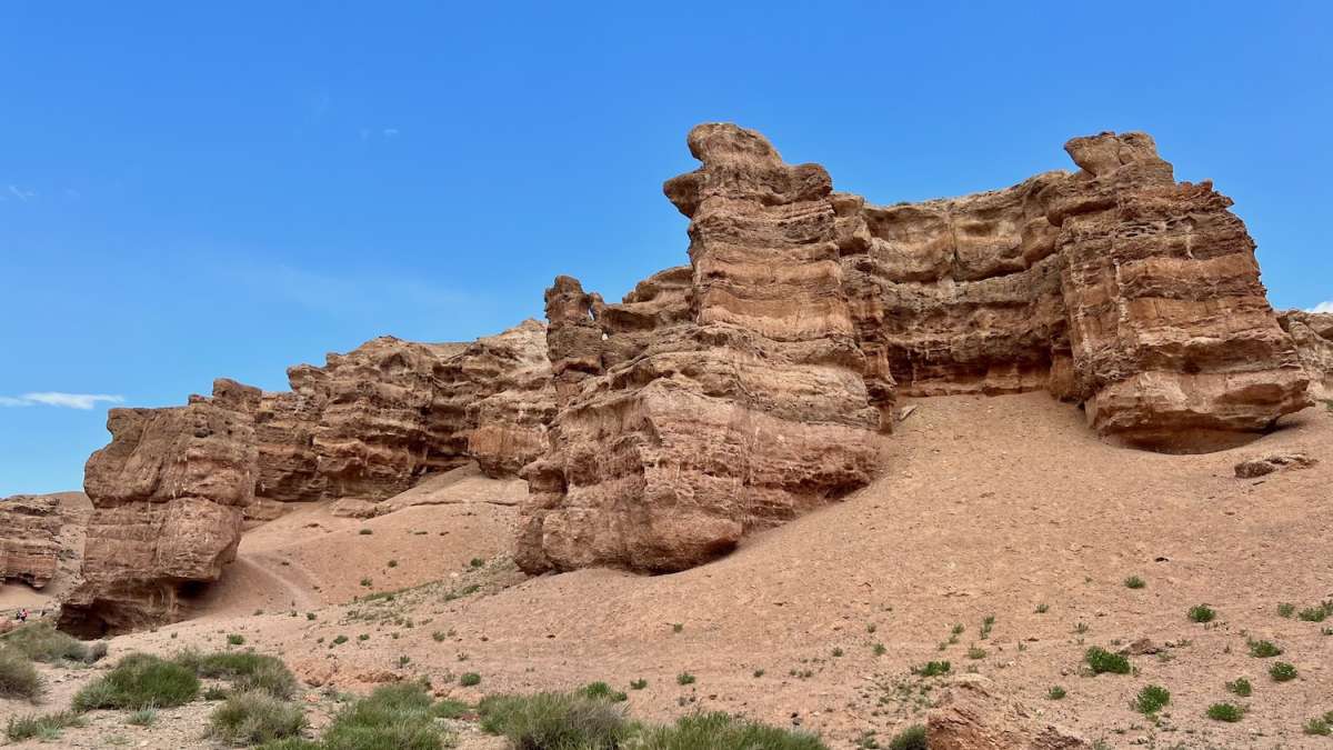 View of the towering and weathered red rock formations of Charyn Canyon against a blue sky, a geological wonder and highlight of Kazakhstan travel.