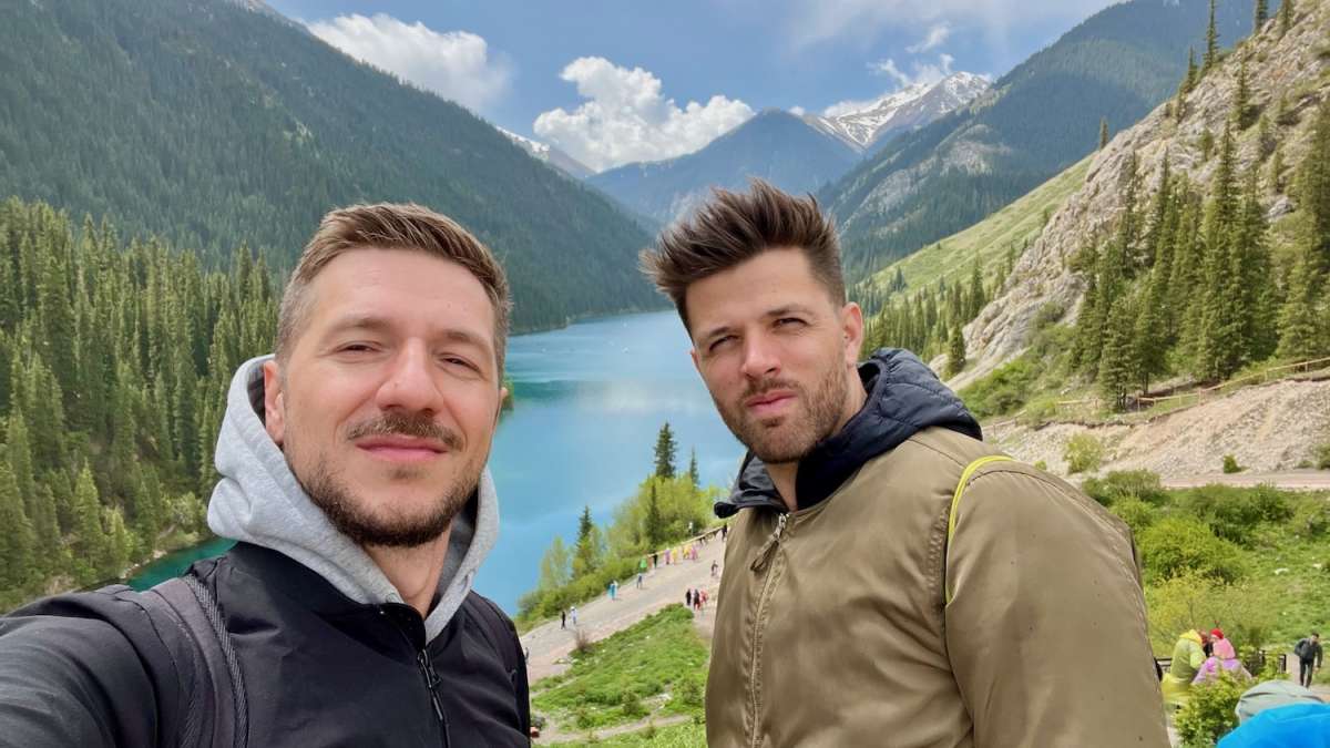 A selfie of two friends with Kolsai Lake and its lush mountainous backdrop, illustrating the joy of exploring Kazakhstan's natural gems.