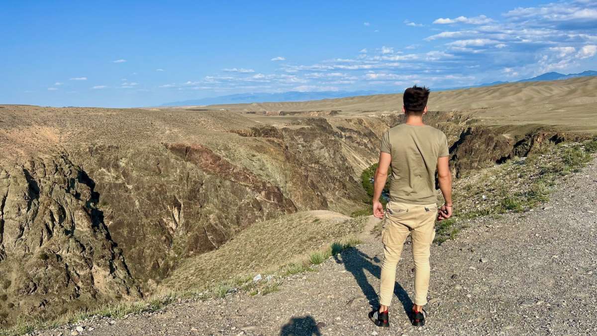 A lone figure walking on a deserted road with dramatic cliffs and expansive views, evoking the solitude and exploration spirit of Kazakhstan travel.