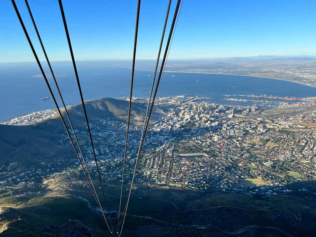 Bird's-eye view from a Table Mountain gondola overlooking the bustling cityscape of gay Cape Town, with the ocean extending to the horizon, showcasing the city's beauty from above.