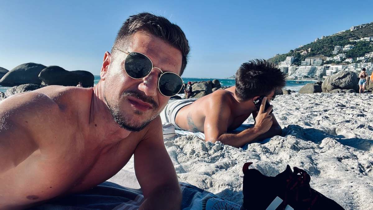 Two men relaxing on Clifton Beach with smartphones and sunglasses, enjoying the sandy shores and gay-friendly atmosphere of Cape Town.