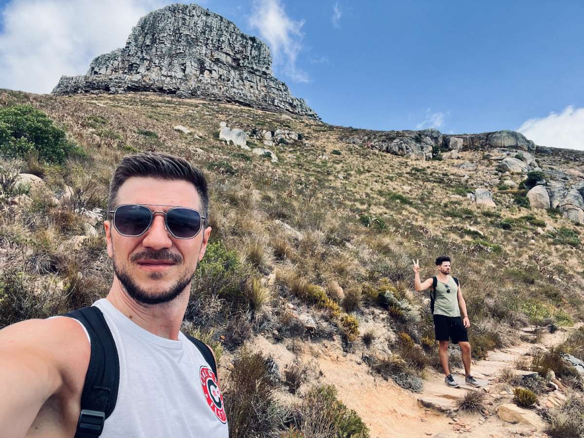 Selfie of two men hiking on Lion's Head in gay Cape Town, with the iconic peak in the background, capturing a moment of adventure in the LGBTQ-friendly destination.