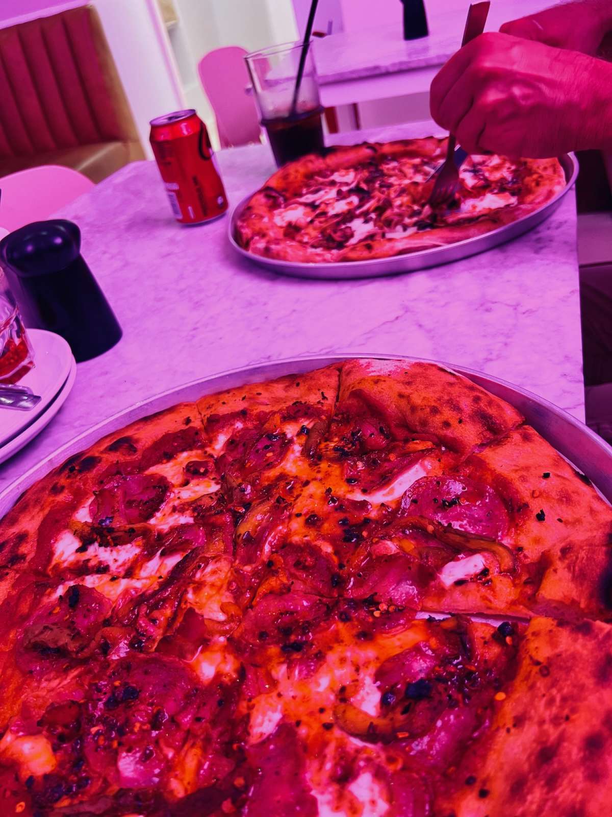 A vibrant photo of gourmet pizzas under a pink hue in a trendy restaurant, representing the diverse culinary scene in gay Cape Town.