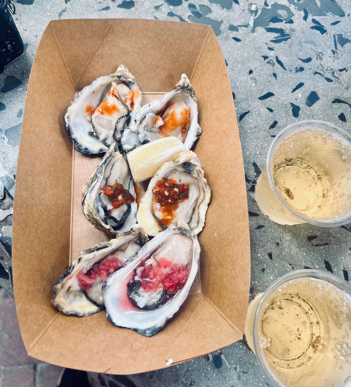 Fresh oysters with condiments on a paper tray, paired with sparkling wine at the Old Biscuit Mill market, a gourmet experience in gay Cape Town