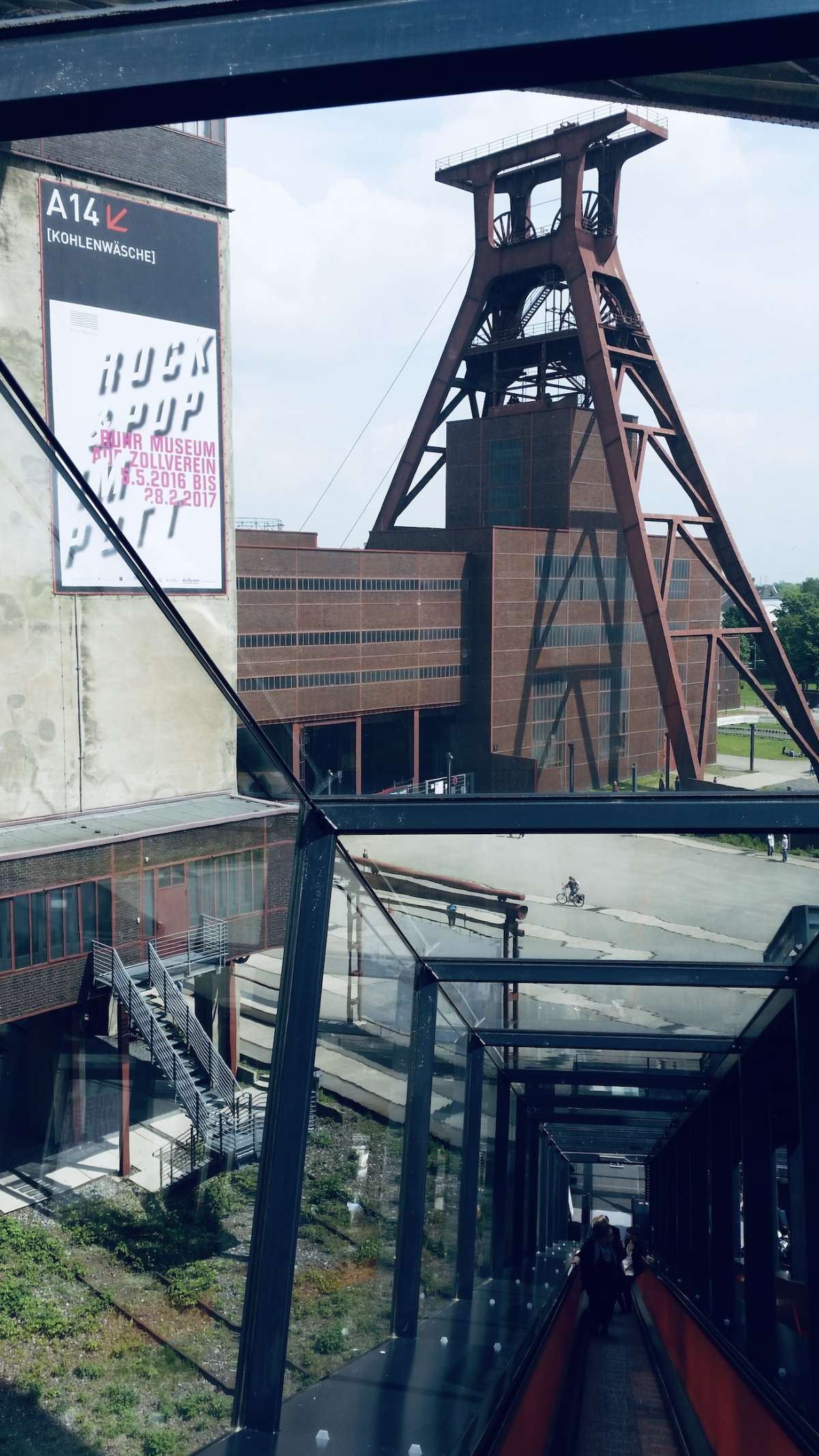 View from a glass-enclosed walkway overlooking the industrial architecture of the Zollverein Coal Mine Industrial Complex in Cologne, a testament to the city's rich industrial heritage and a nod to gay Cologne's blend of history and modernity.