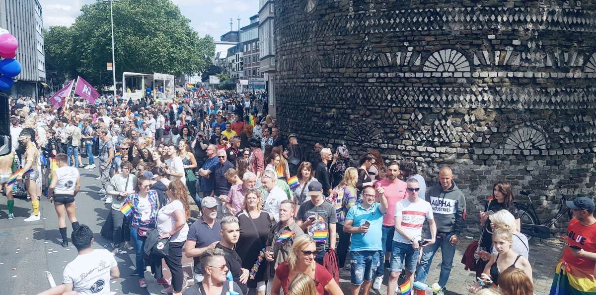 A crowded scene from Cologne's gay pride parade, with people of all ages celebrating diversity and equality on a sunny day, embodying the inclusive spirit of gay Cologne.