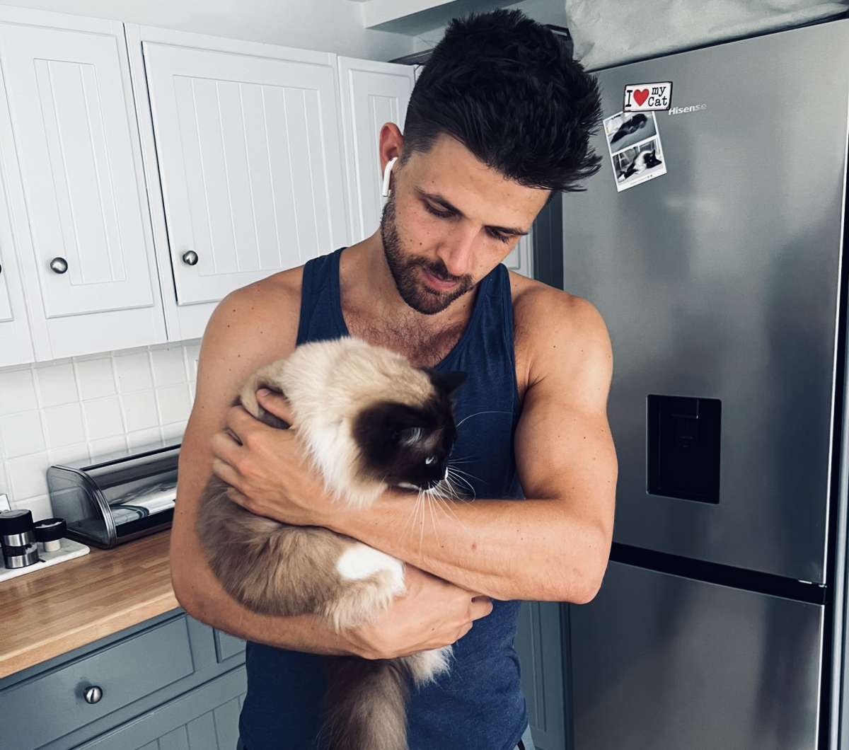 A tender moment between a man and his cat in a modern kitchen, depicting the intimate domestic life within the Gay London community.