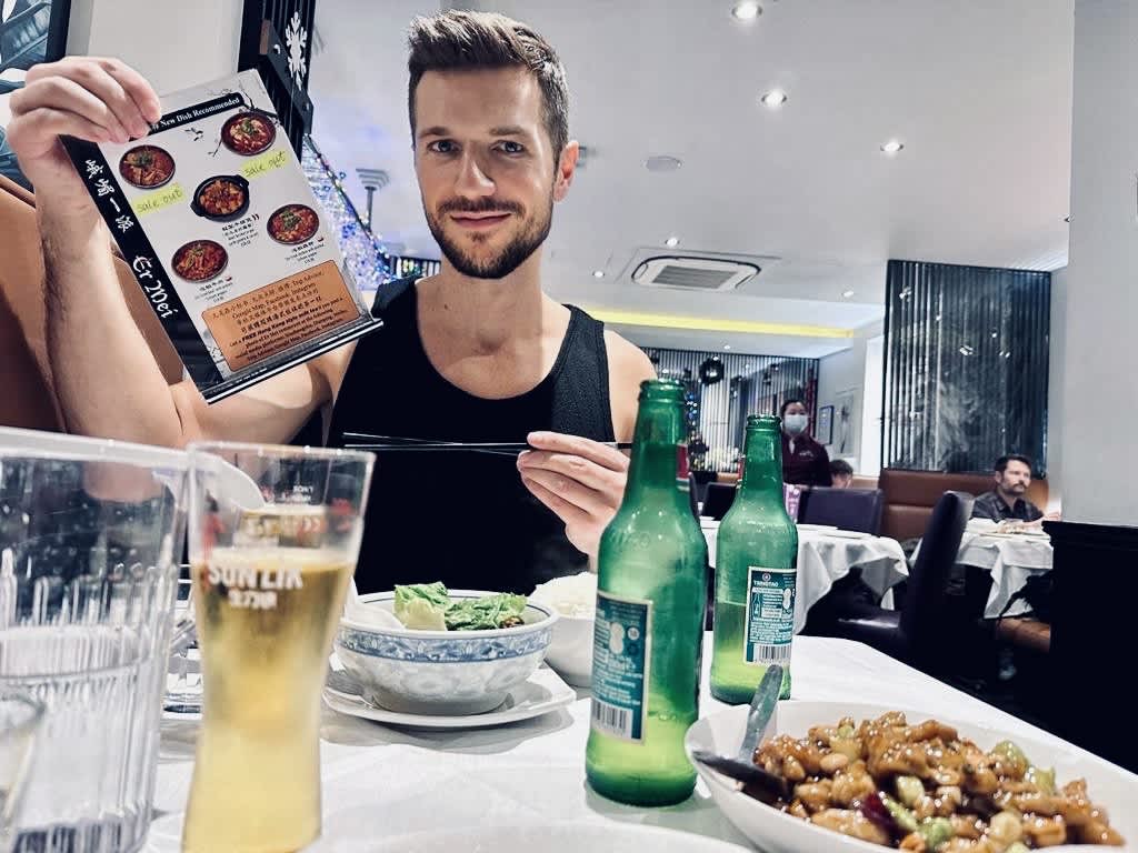 A man smiling while holding a menu at Erméi Sichuan, representing the diverse culinary experiences within Gay London.