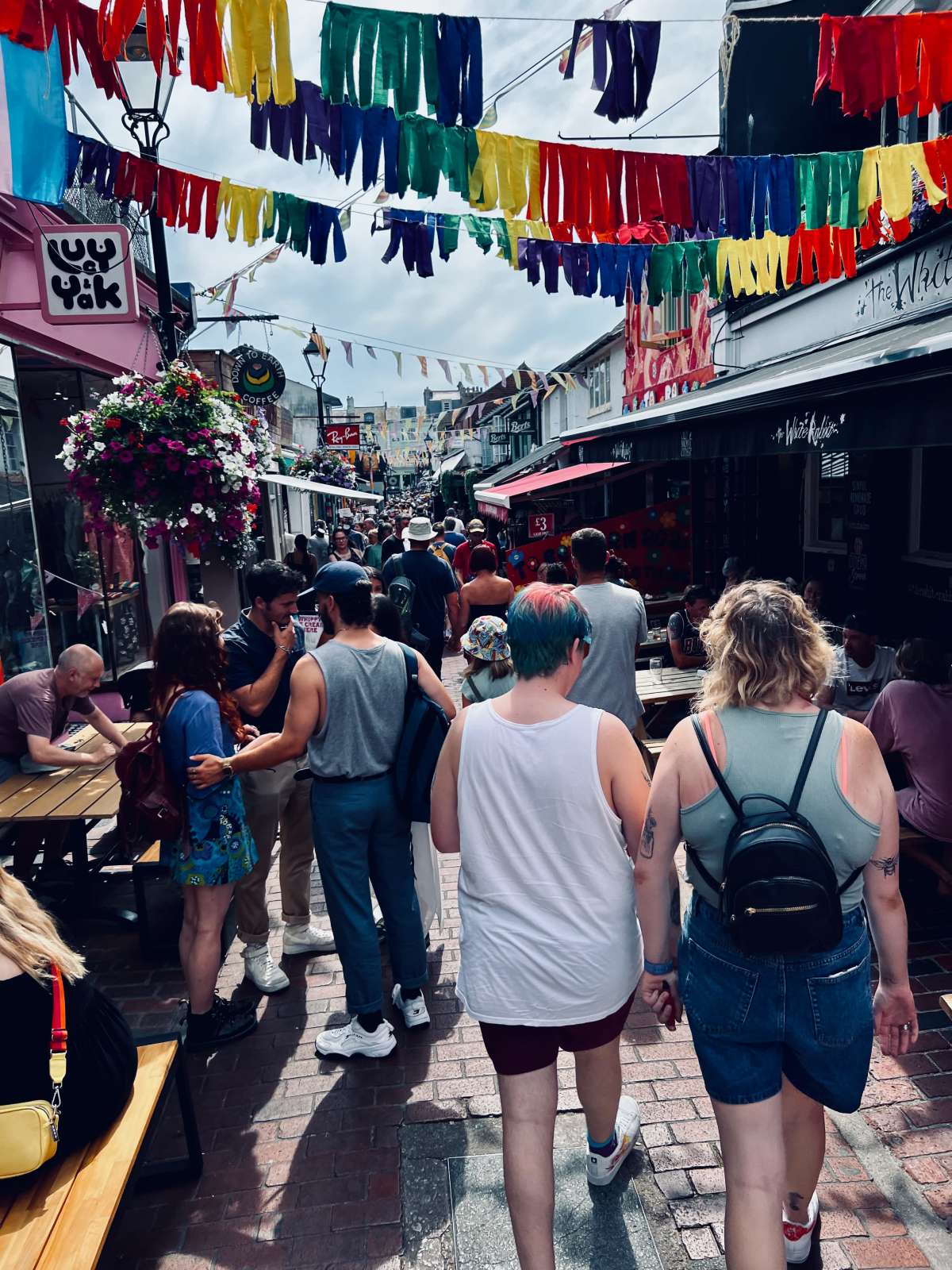 Pedestrians on a vibrant street decorated with rainbow flag in Gay Brighton.