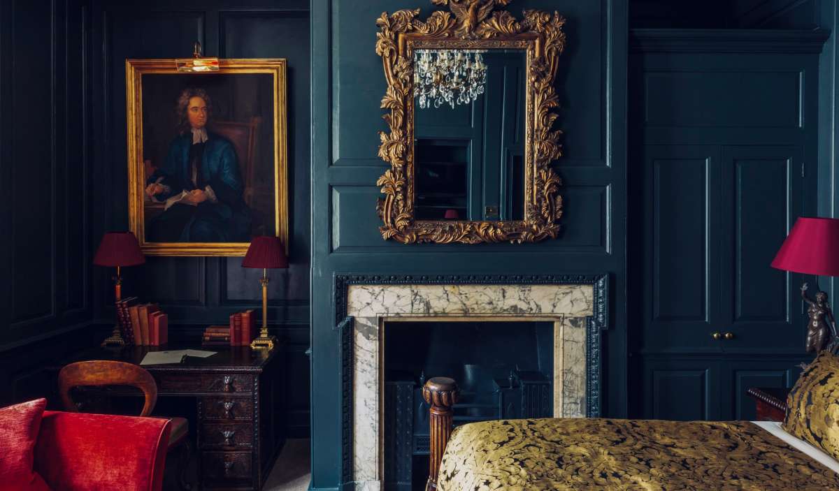 An opulent bedroom with deep blue walls and gold accents, reflecting the luxury and historical beauty found in Gay London's boutique accommodations.