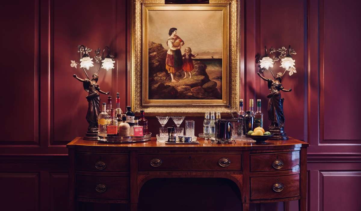 An ornate traditional liquor cabinet with a painting above it, illustrating the refined and cultured feel of Batty Langley's Hotel in London