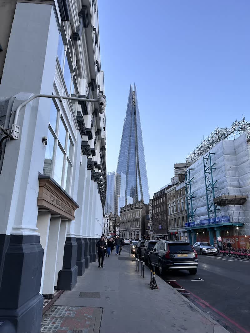 The Shard piercing the blue sky, as seen from a bustling London street, a testament to the city's architectural marvels and Gay London's urban charm.