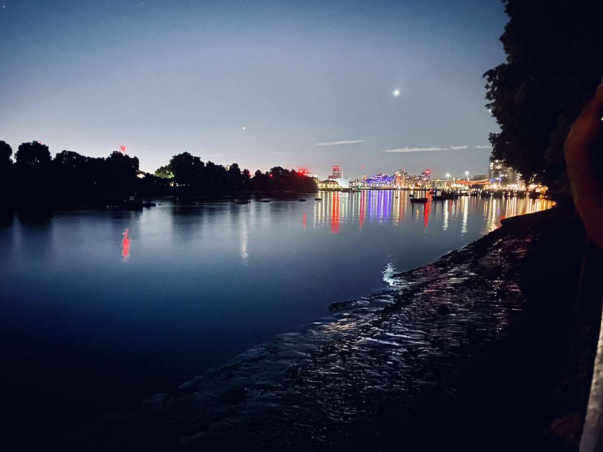 Nighttime view of the Thames with the glittering lights of Chelsea in the distance, a serene Gay London riverside experience.