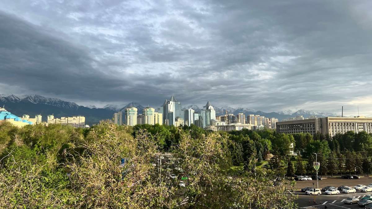 Panoramic view of Almaty's skyline with modern buildings juxtaposed against the backdrop of the snow-capped Zailiysky Alatau mountain range in Kazakhstan.