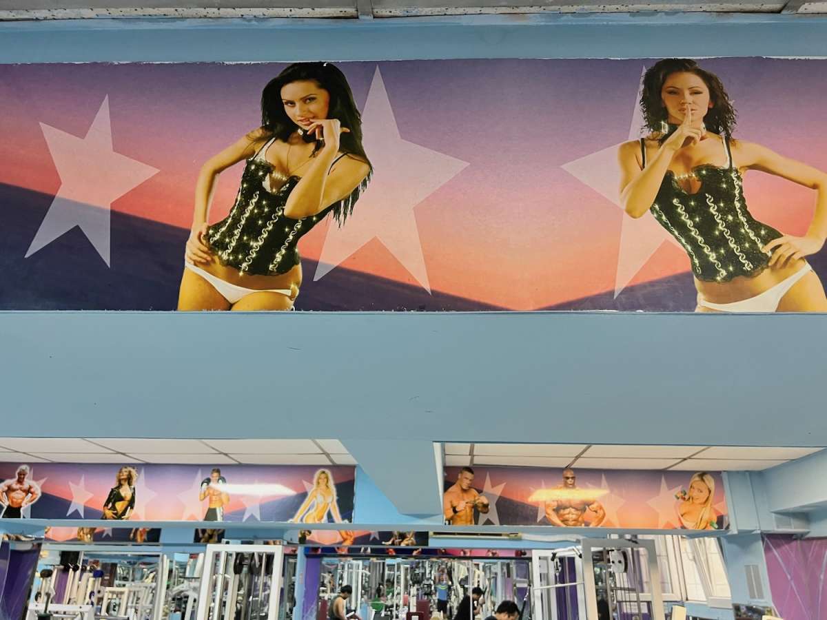 Interior of a gym in Almaty, Kazakhstan, decorated with colorful posters featuring fitness models, highlighting a vibrant workout atmosphere.