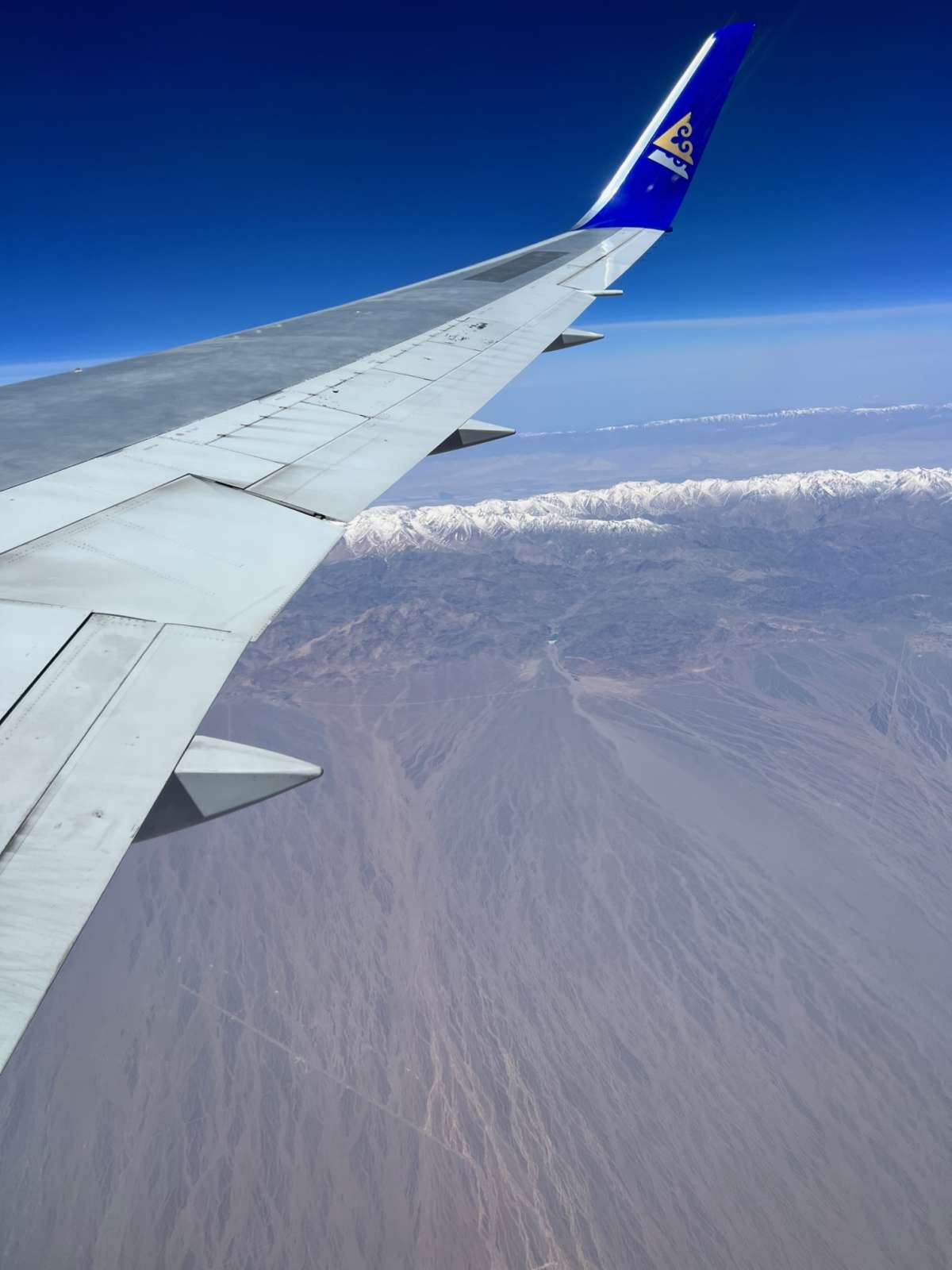View from an Air Astana airplane's wing as it flies over the rugged, snowy peaks near Almaty, Kazakhstan, showcasing the vast and varied terrain.