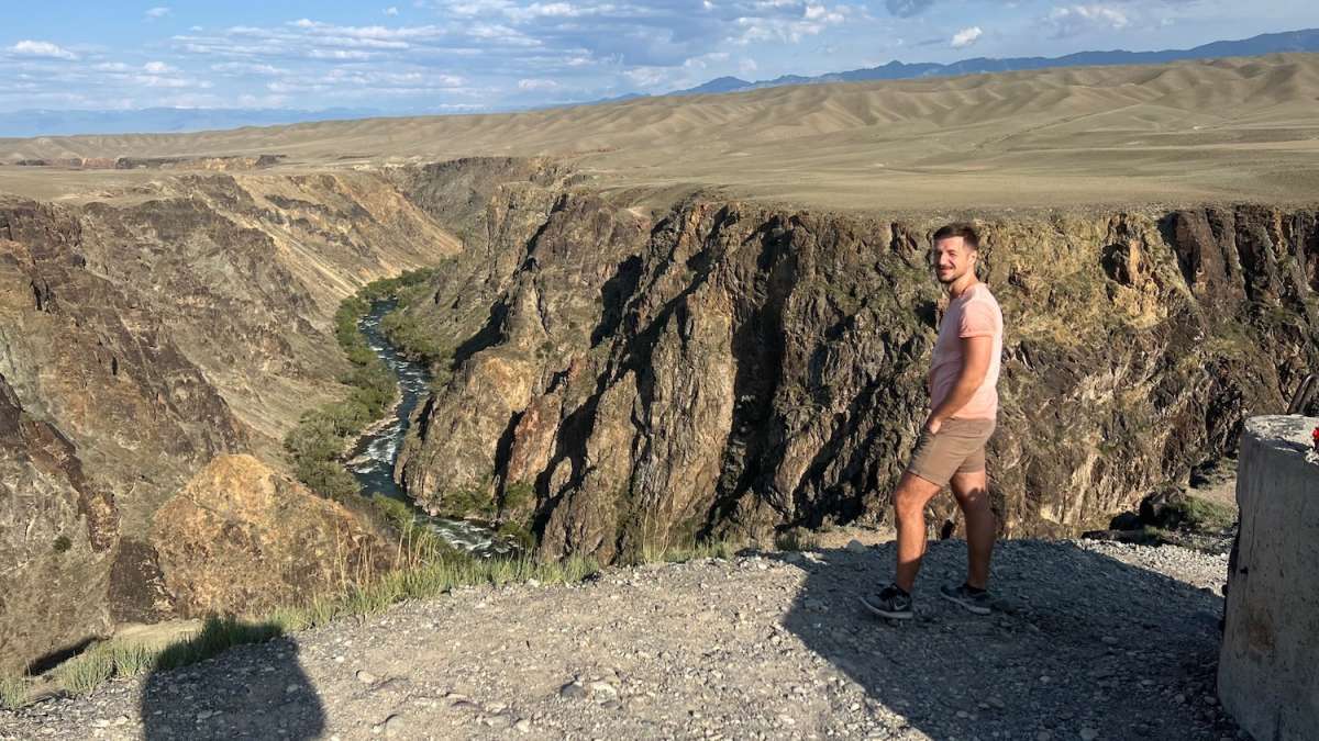 Scenic view of a deep canyon with a river meandering through it, under the vast open skies of Kazakhstan, near Almaty.