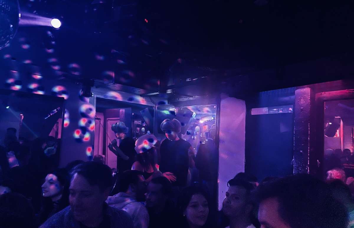 Energetic party atmosphere inside a gay Frankfurt club (Pink Club) with colorful lights reflecting off bubbles, highlighting the city's active LGBTQ nightlife.