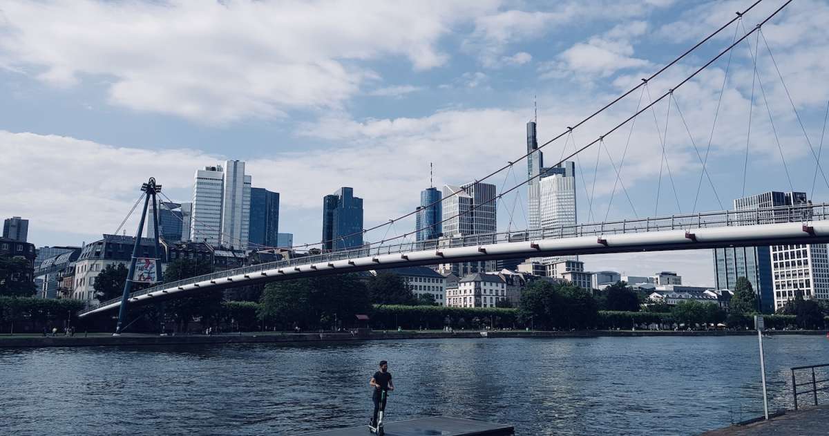 Sleek pedestrian bridge spanning the Main River in gay Frankfurt with a backdrop of the city's financial district skyscrapers under a cloudy sky.