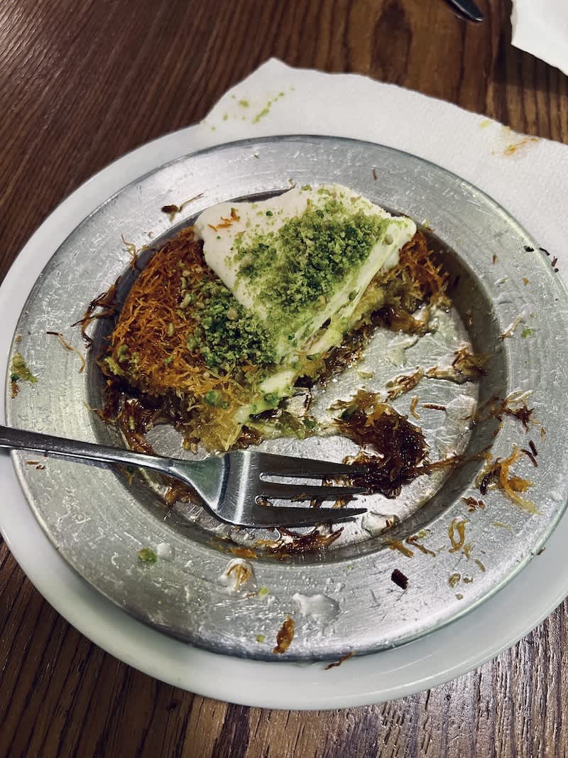 Half-eaten plate of Künefe at Damla in Cologne, displaying a fusion of shredded wheat, sweet syrup, and pistachios, inviting food enthusiasts to explore one of the best restaurants in Cologne for Middle Eastern desserts.