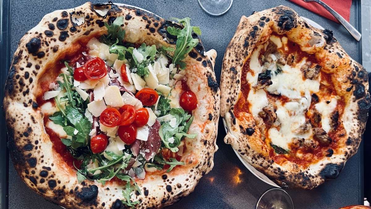 Close-up of two Neapolitan pizzas from Toto & Pepino, one topped with fresh arugula, cherry tomatoes, and shaved parmesan, the other with bubbly mozzarella and mushrooms, exemplifying the culinary delights at one of the best restaurants in Cologne.