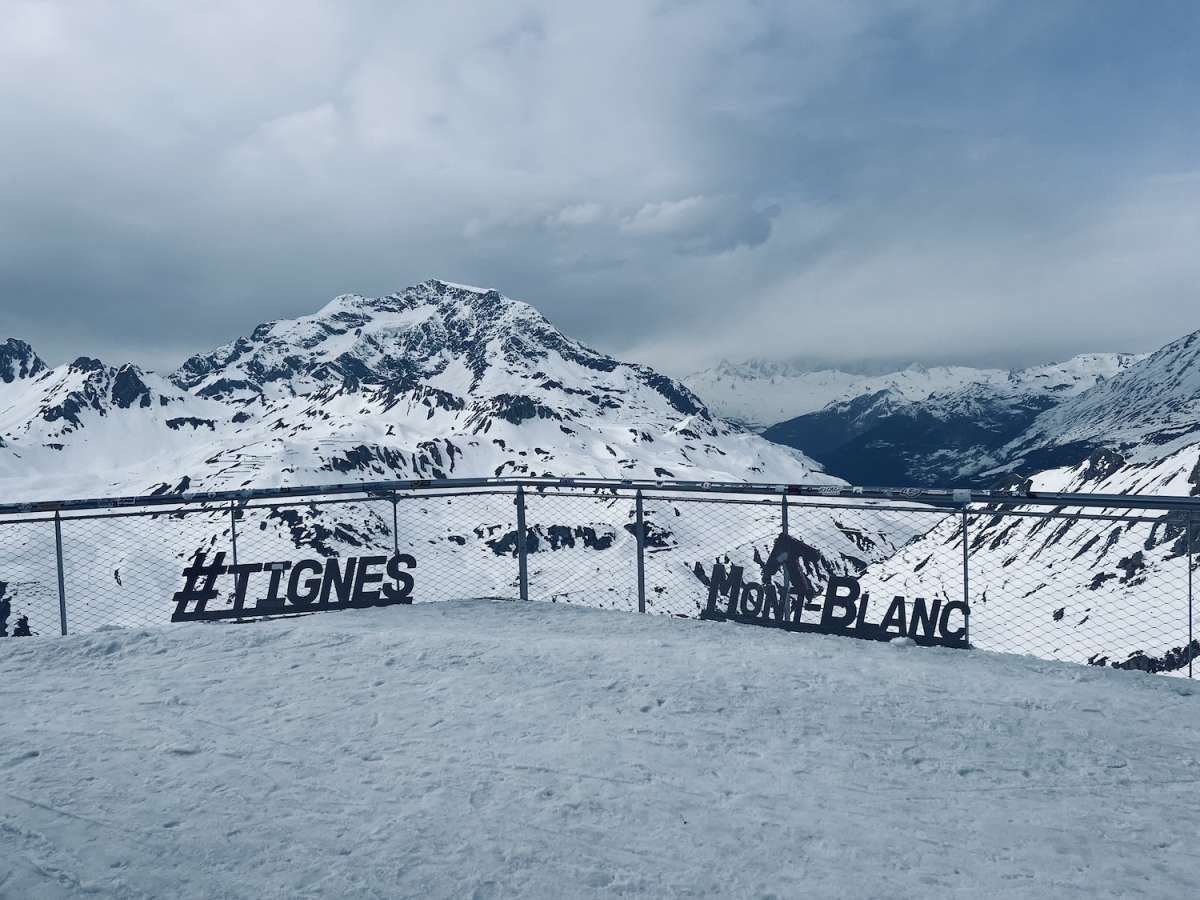 Iconic view from Tignes showing hashtag signs '#TIGNES' and 'MONT BLANC' against a panoramic backdrop of the majestic, snow-capped Alps during Gay Ski Week.
