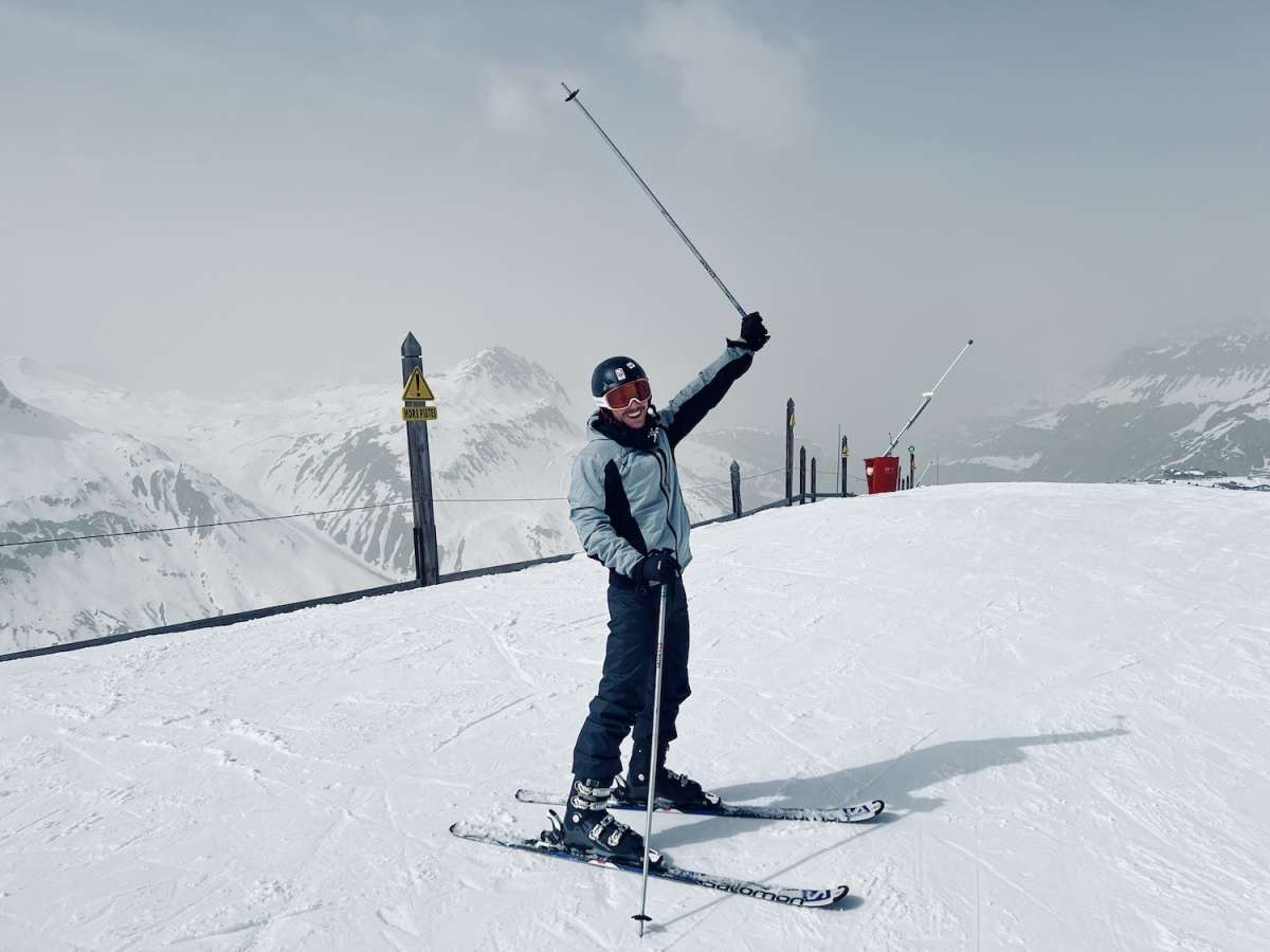 An enthusiastic skier with arms triumphantly raised on the snowy slopes of Tignes, celebrating the vibrant spirit of Gay Ski Week against a backdrop of expansive mountain views.