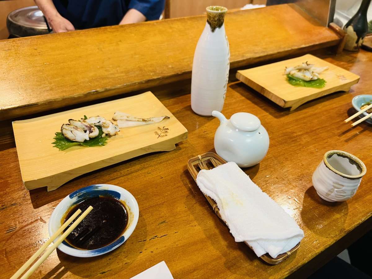 A selection of Japanese sushi including squid and other seafood on a wooden platter with a sake set, epitomizing Nagasaki's culinary arts.