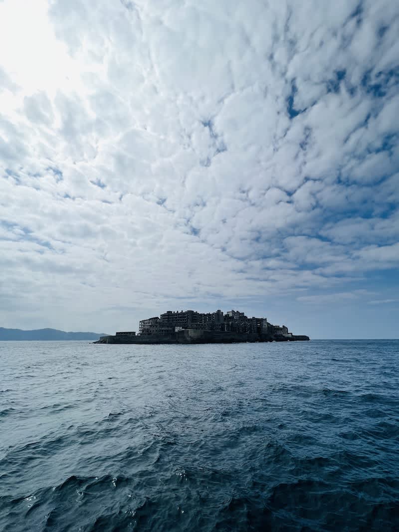 The abandoned Hashima Island, also known as Gunkanjima, off the coast of Nagasaki, under a cloudy sky, evoking historical intrigue.